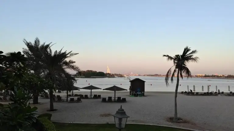 a beach with a building and palm trees and the ocean at 2 Bedroom beach front apartment in Dubai