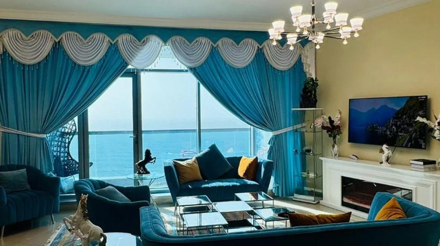a living room with a large blue couch and blue curtains at Ajman Luxurious Holiday Homes in Ajman