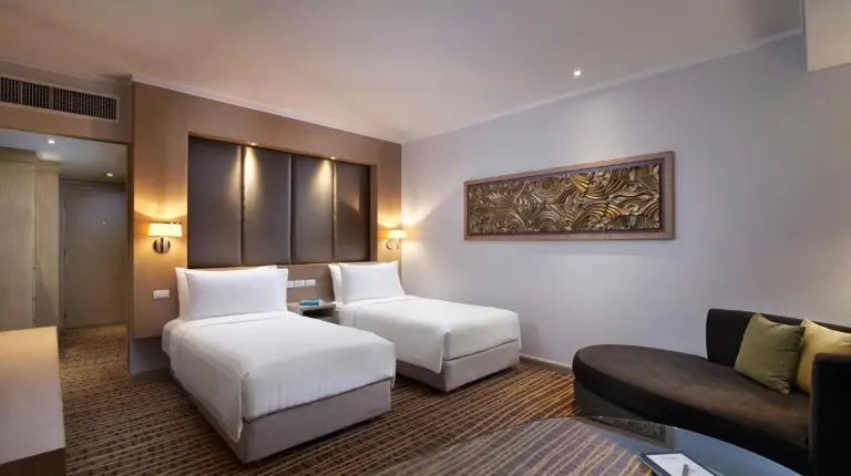 a hotel room with a couch and a desk and a window at Amari Bangkok in Bangkok