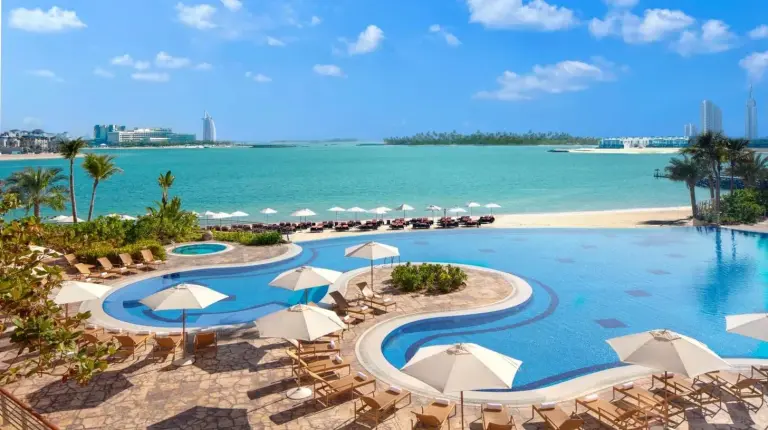 ein Resort‑Pool mit Liegestühlen und Sonnenschirmen und dem Ozean im Andaz Family Suites by Hyatt- Palm Jumeirah in Dubai