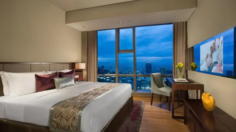 a bedroom with a bed and a desk and a large window at Ascott Kuningan Jakarta in Jakarta