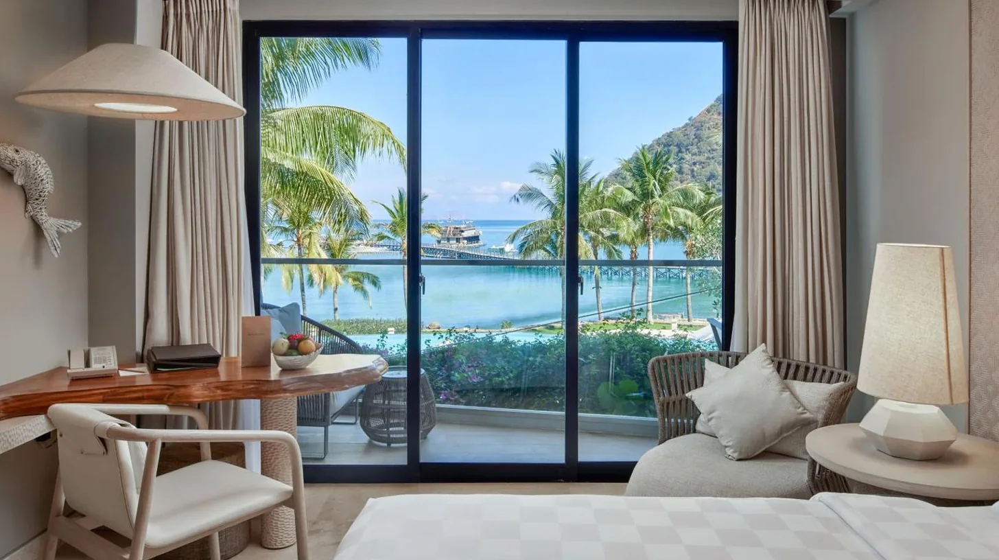 a bedroom with a bed and a desk and a large window at AYANA Komodo Waecicu Beach in Labuan Bajo
