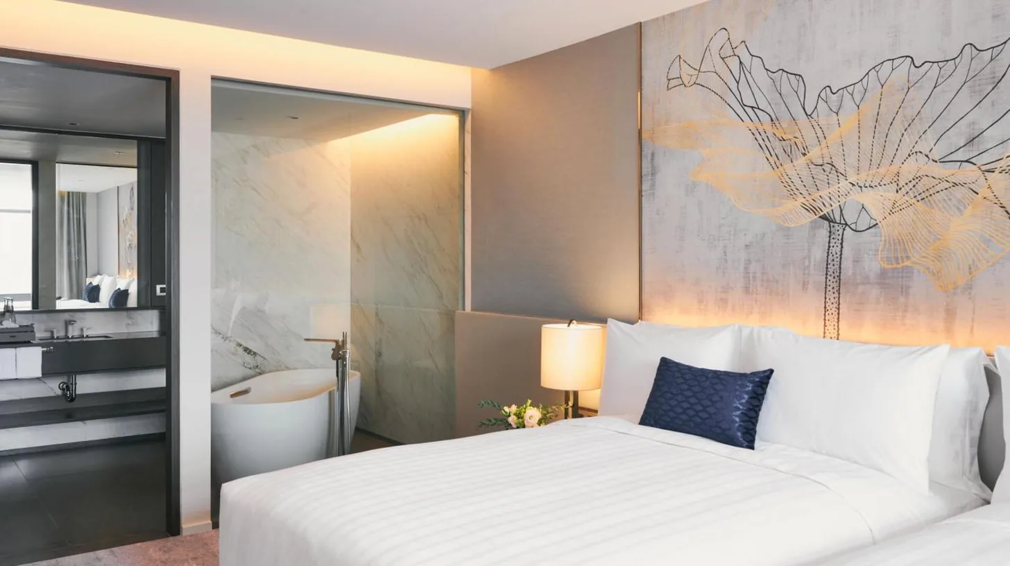 a bedroom with a large white bed and a bathroom at Chatrium Grand Bangkok in Bangkok