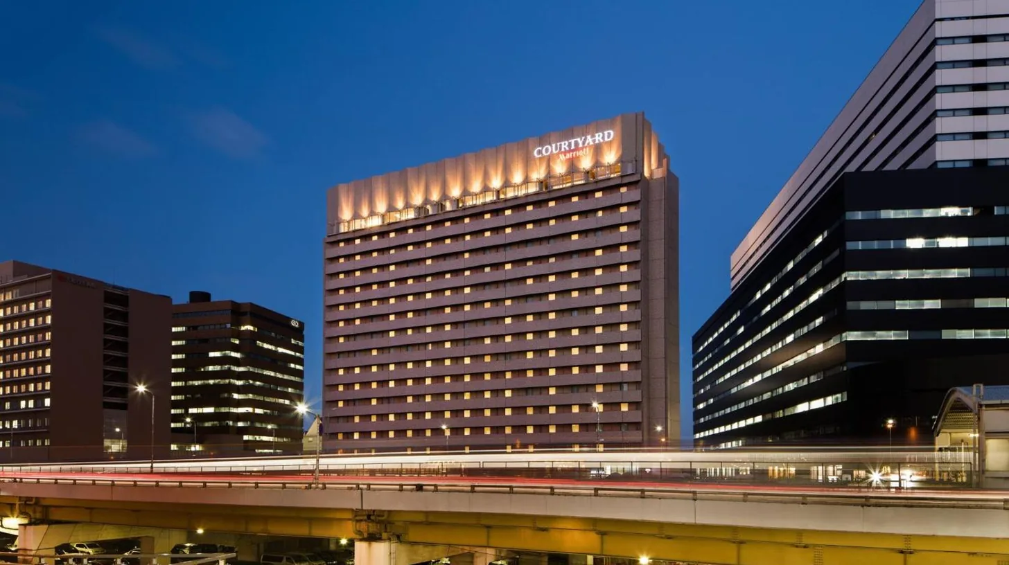 a tall building with a train in front of it at Courtyard by Marriott Shin-Osaka Station in Osaka