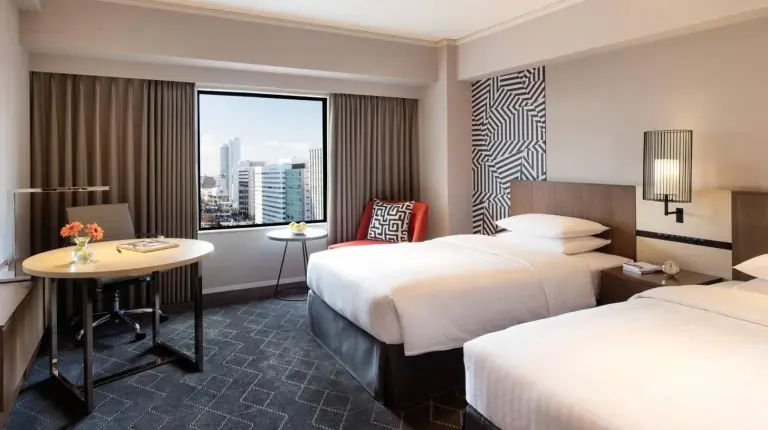 a hotel room with two beds and a table and a window at Courtyard by Marriott Shin-Osaka Station in Osaka