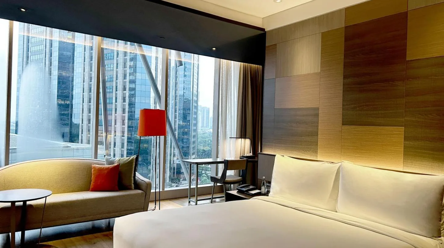 ein Schlafzimmer mit einem Bett, einer Couch und großem Fenster im Discovery SCBD Jakarta in Jakarta