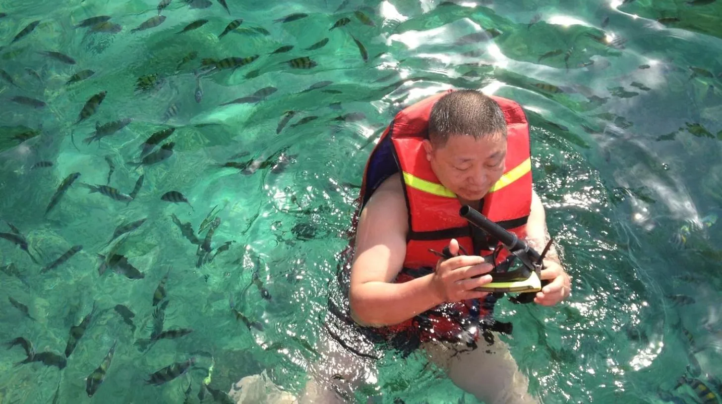 a man in the water taking a picture of fish at Downtown Oasis 芭提雅市中心独栋泳池别墅 A 5卧6卫 KTV BBQ 芭提雅海滩步行街500m in Pattaya South