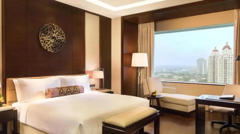 a bedroom with a bed and a desk and a window at Fairmont Jakarta in Jakarta