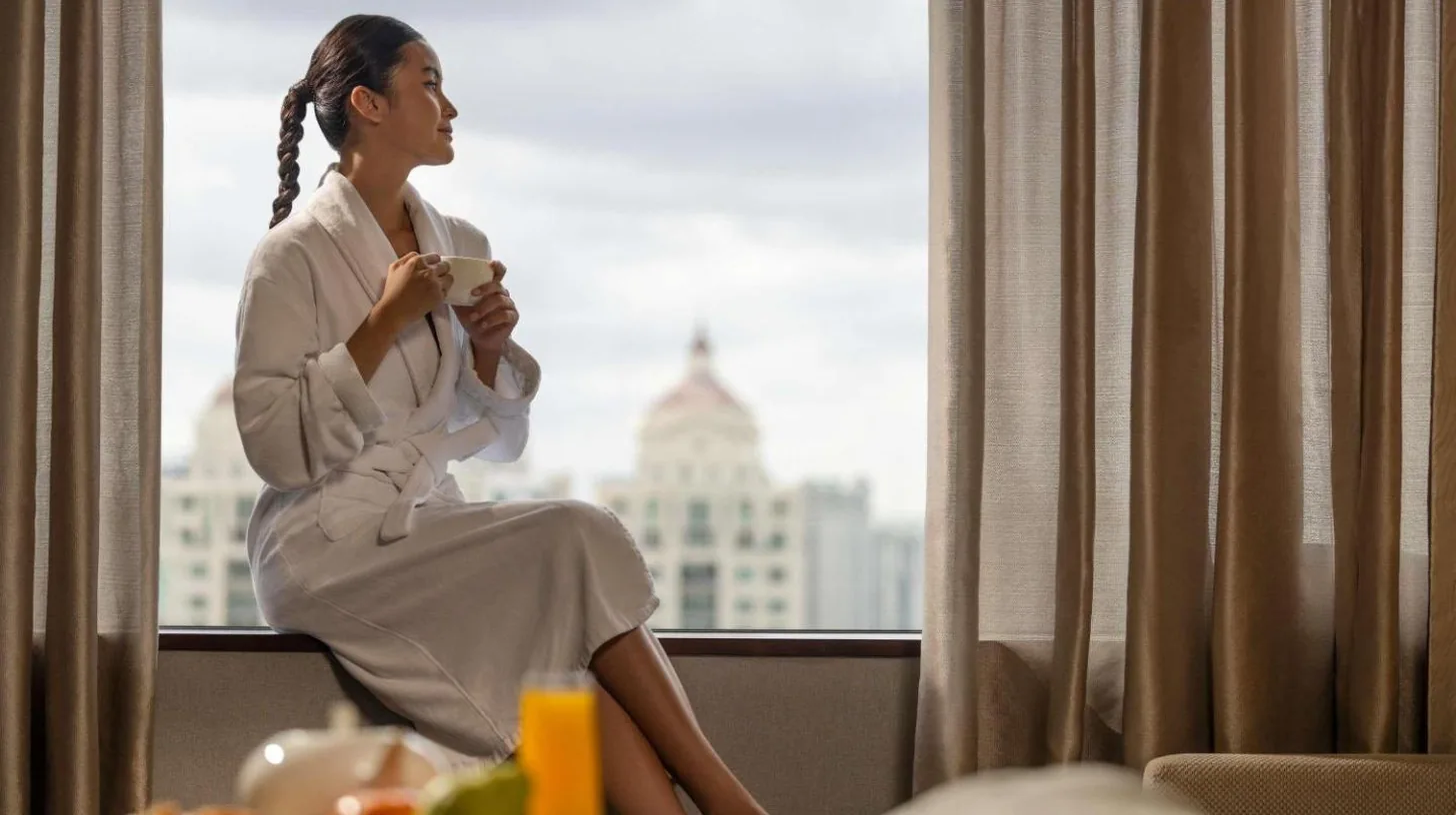 a woman sitting in a hotel room looking out the window at Fairmont Jakarta in Jakarta