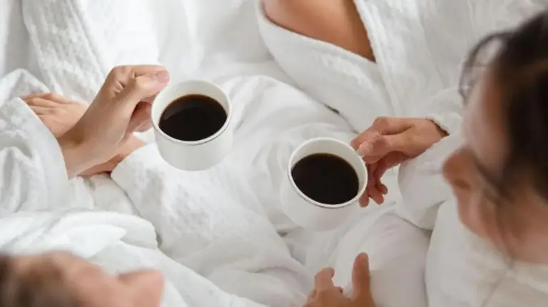 dos personas acostadas en la cama con dos tazas de café en Four Seasons Hotel Bangkok at Chao Phraya River en Bangkok