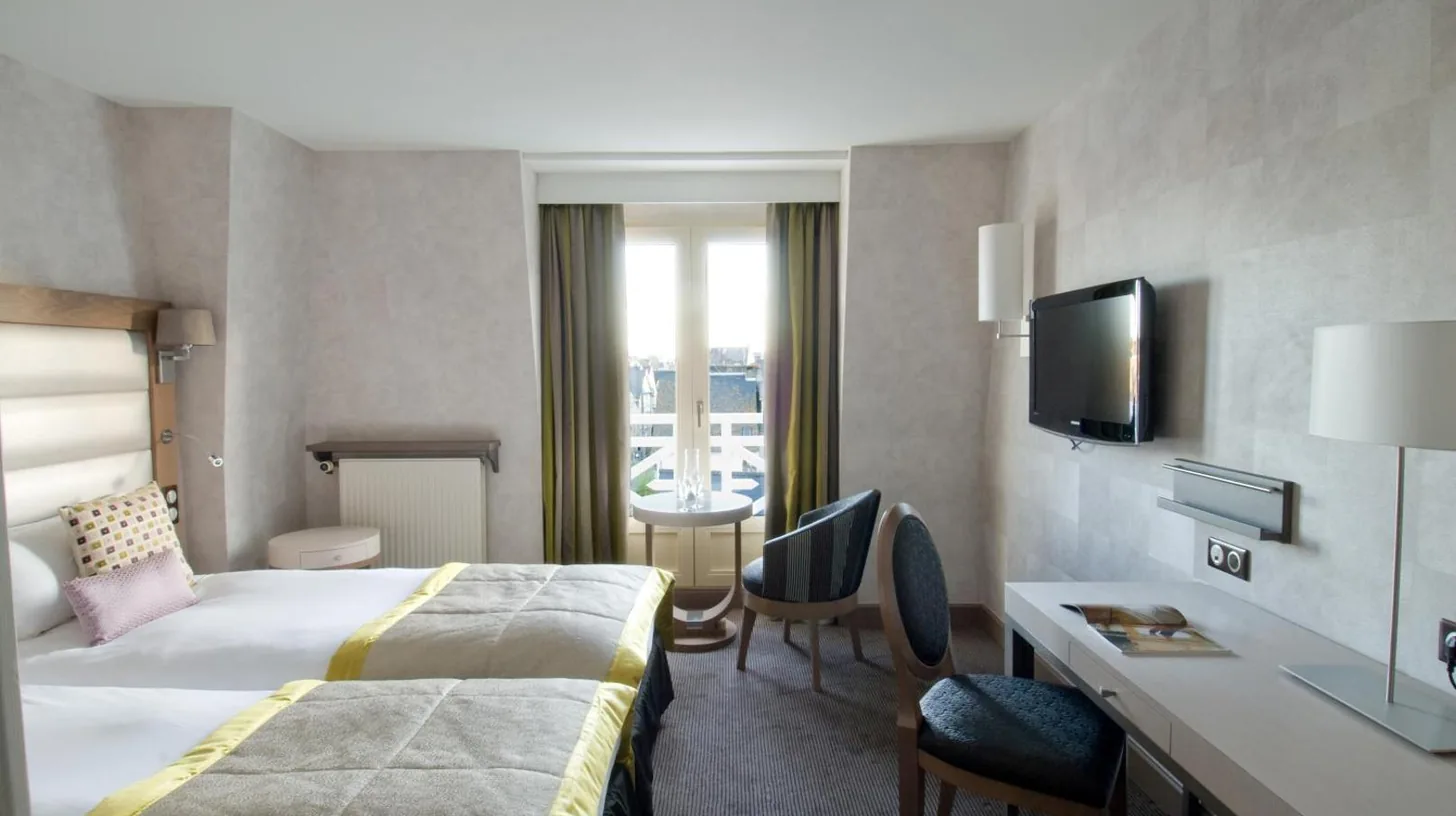 a hotel room with a bed and a desk and a television at Grand Hôtel Des Thermes in Saint Malo