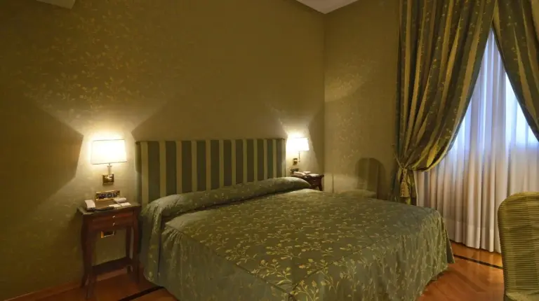 a bedroom with a bed and two lamps and a window at Grand Hotel Vesuvio in Naples