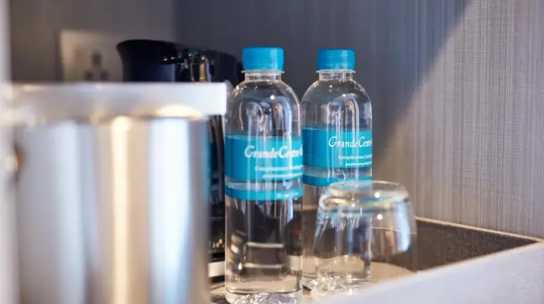 three bottles of water sitting on a shelf with glasses at Grande Centre Point Pattaya in Pattaya Central