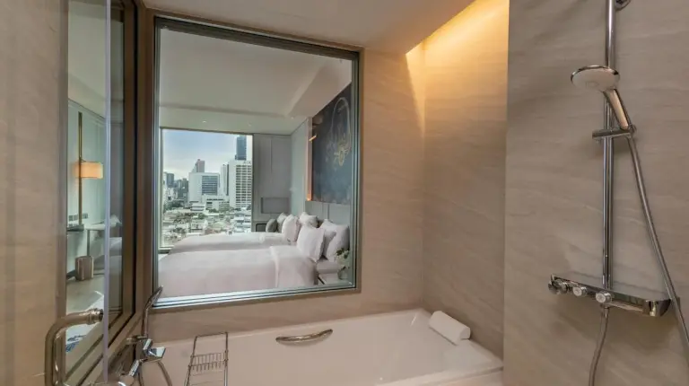 a bathroom with a bath tub and a bedroom at Grande Centre Point Surawong Bangkok in Bangkok
