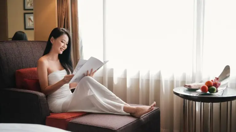 a woman sitting in a chair reading a book at Hilton Bangkok Grande Asoke in Bangkok