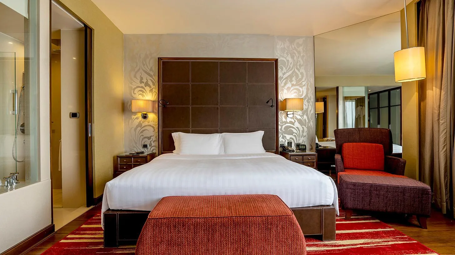 a bedroom with a large bed and a red chair at Hilton Bangkok Grande Asoke in Bangkok