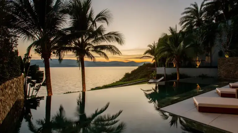 a swimming pool with palm trees and a view of the water at Kerem Luxury Beachfront Villas in Choeng Mon Beach