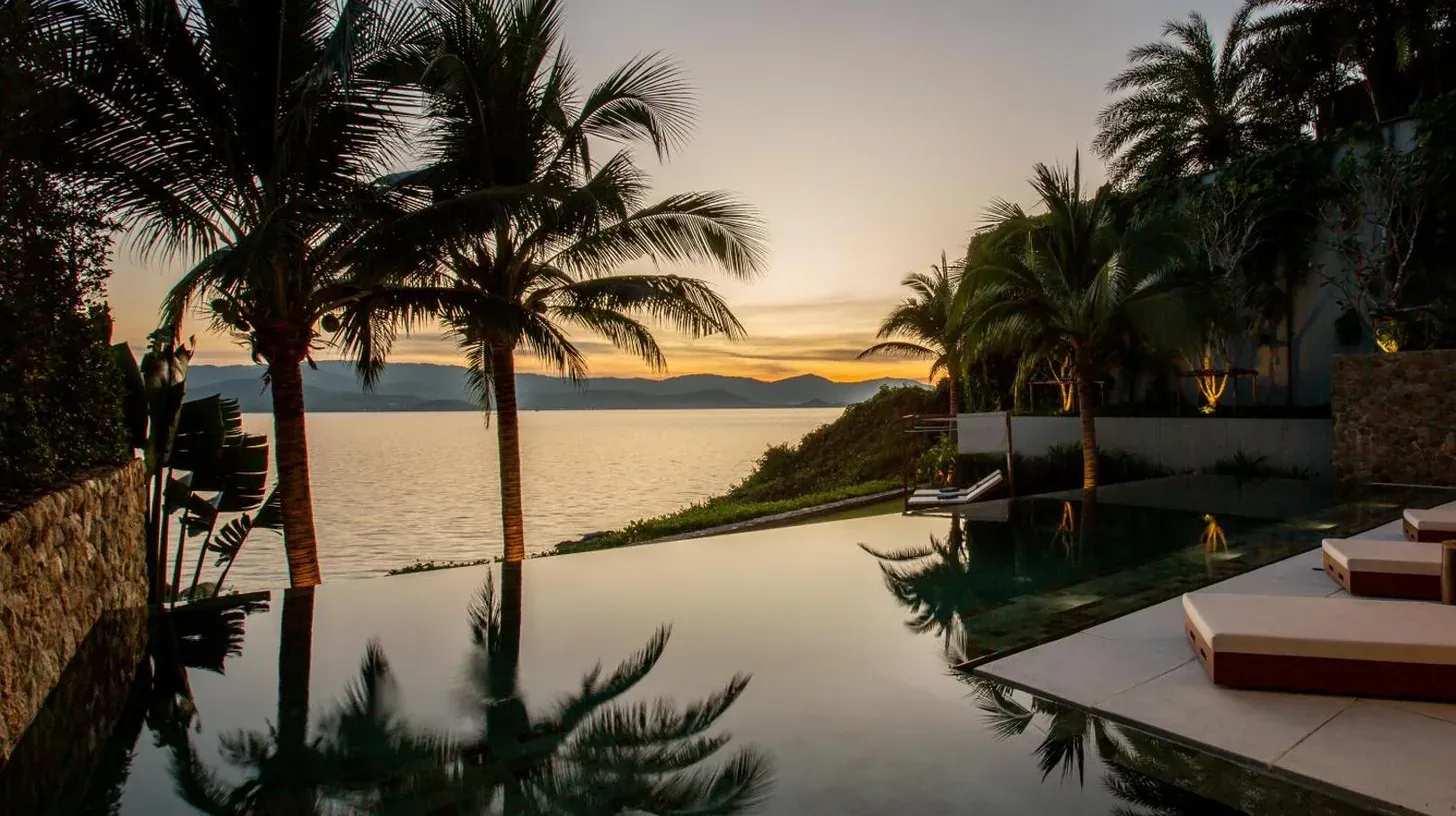 a swimming pool with palm trees and a view of the water at Kerem Luxury Beachfront Villas in Choeng Mon Beach