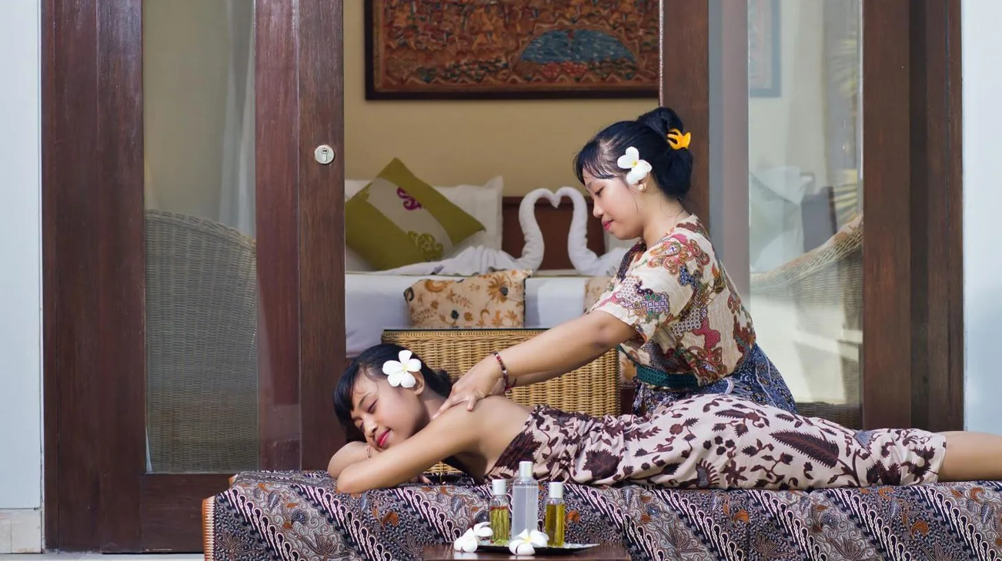 a woman cutting a girls hair on a bed at The Buah Bali Villas in Seminyak