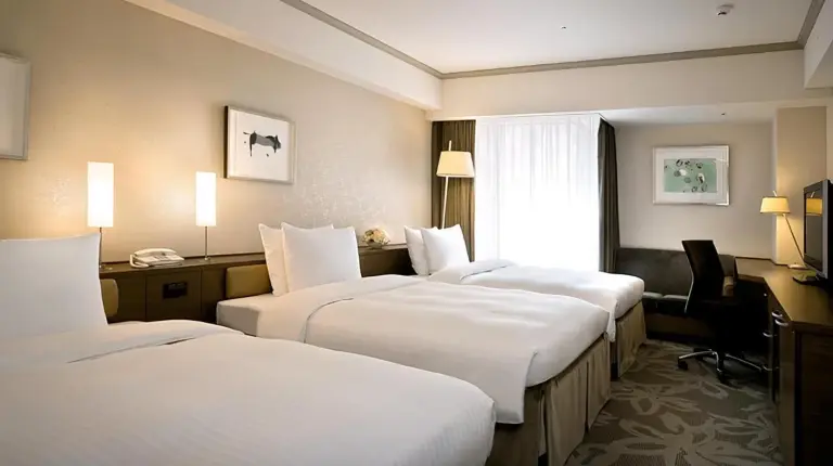 a hotel room with three beds and a desk at Hotel Nikko Fukuoka in Fukuoka