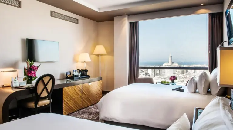 a hotel room with two beds and a desk and a window at Kenzi Tower Hotel in Casablanca
