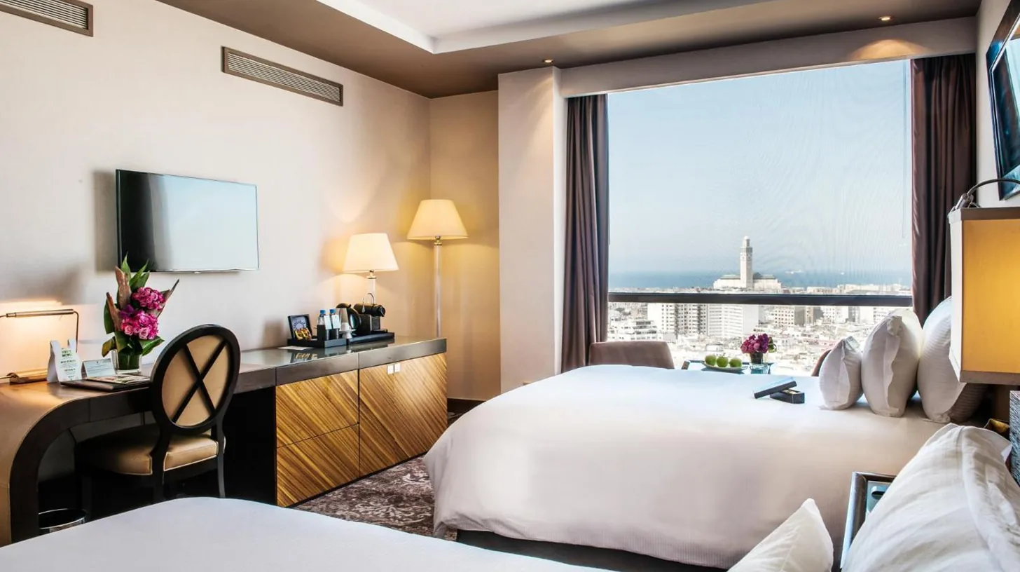 a hotel room with two beds and a desk and a window at Kenzi Tower Hotel in Casablanca