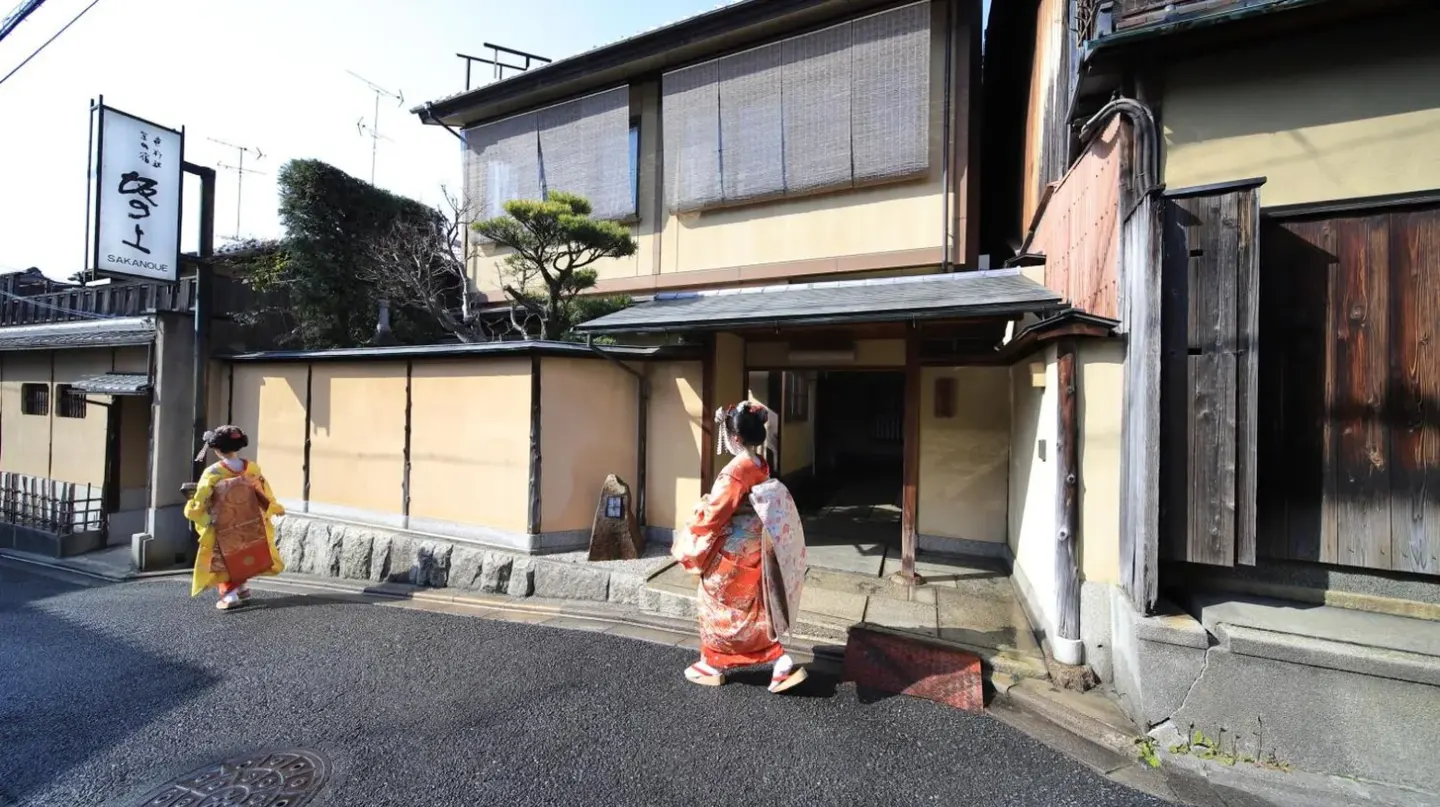 two women walking down a street next to a building at Kyoto Ryokan SAKANOUE in Kyoto