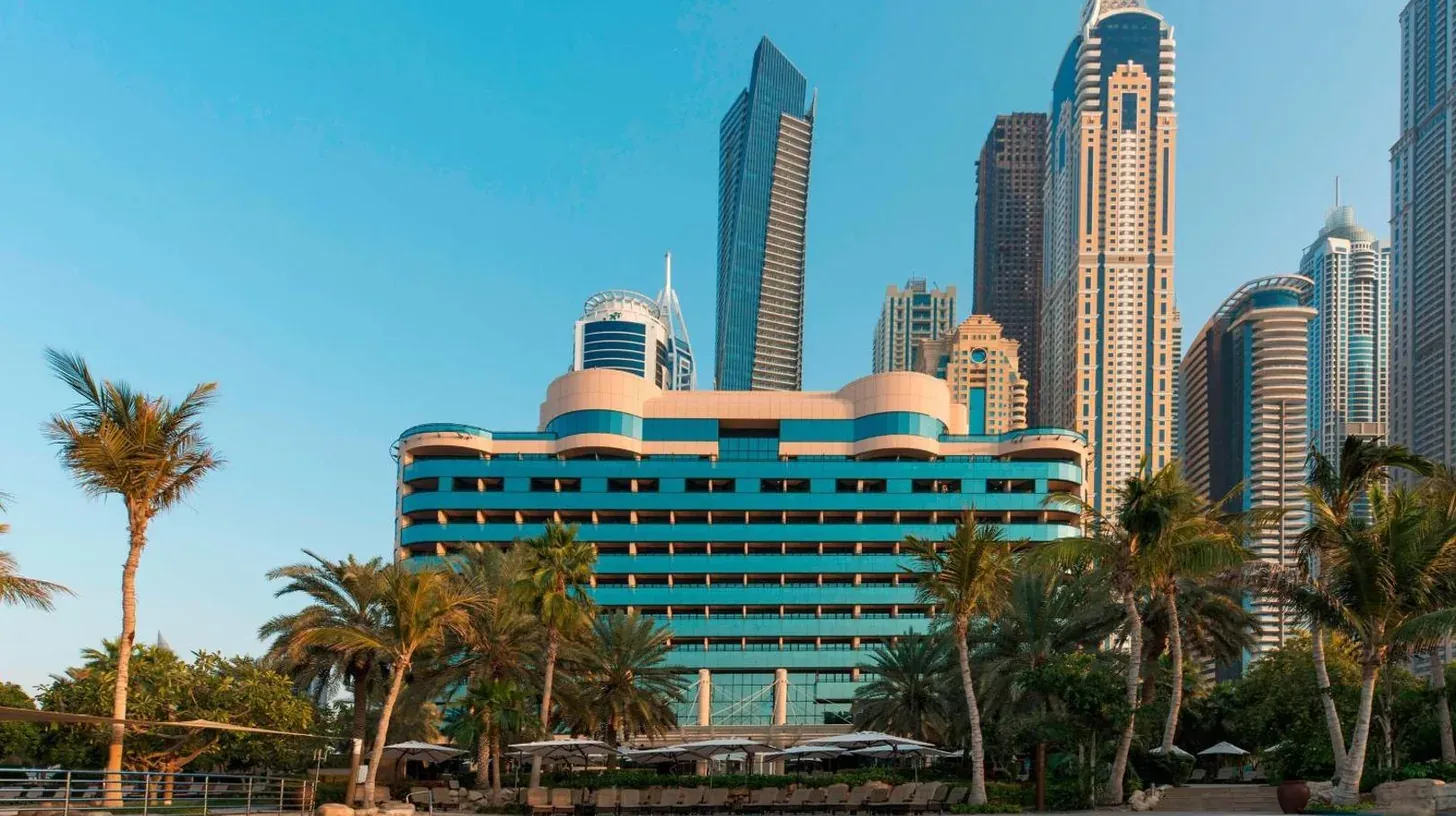 a hotel with palm trees in front of a city at Le Meridien Mina Seyahi Beach Resort & Waterpark in Dubai