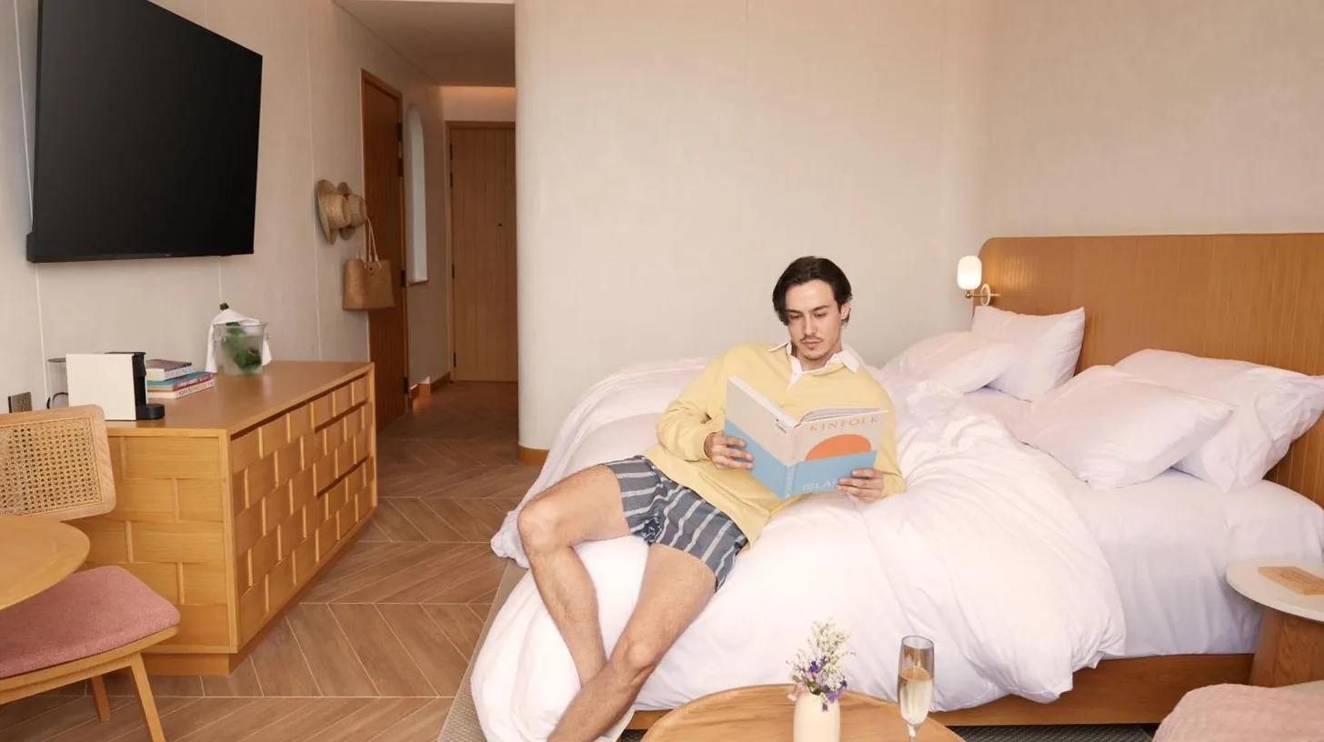 a man sitting on a bed reading a book at Marasca Samui - Small Luxury Hotels of the World in Chaweng