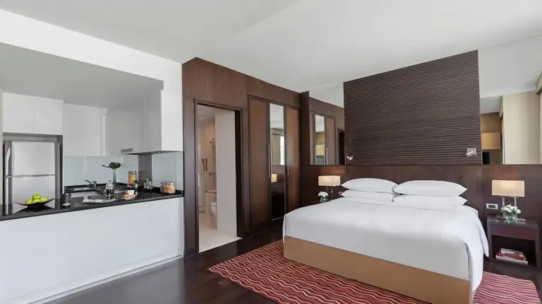a bedroom with a large white bed and a kitchen at Marriott Executive Apartments Sukhumvit Park