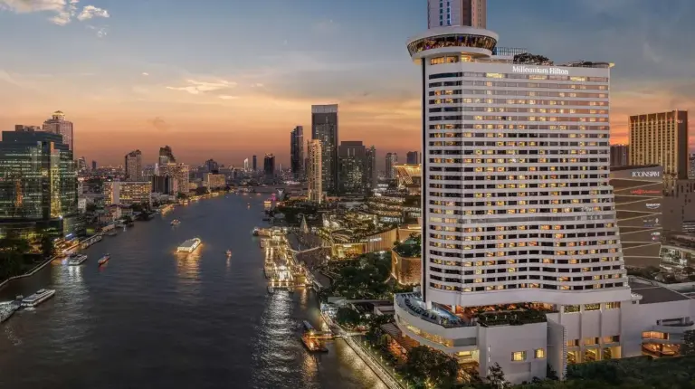 a tall building next to a river in a city at Millennium Hilton Bangkok in Bangkok