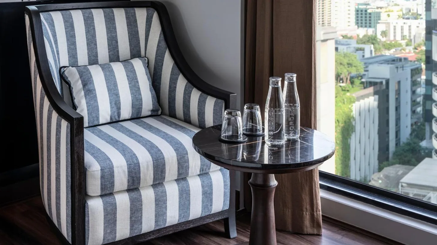 a chair with a table in a room with a window at Montraj Continent Sukhumvit Bangkok in Bangkok