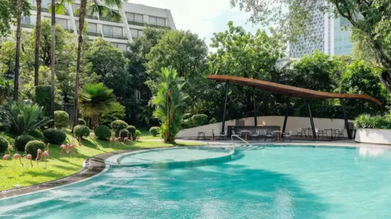 a swimming pool in a park with chairs and trees at Mövenpick BDMS Wellness Resort Bangkok in Bangkok