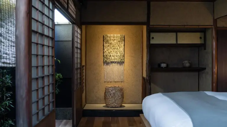 a bedroom with a bed and a lamp on the wall at Nazuna Kyoto Gosho in Kyoto