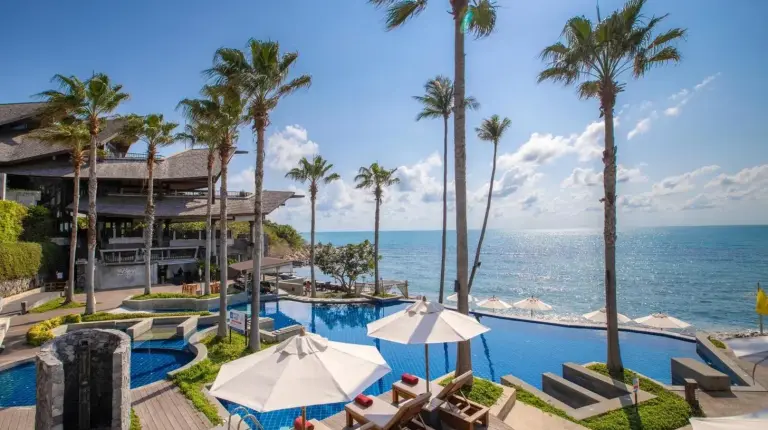 a resort pool with chairs and palm trees and the ocean at Nora Buri Resort & Spa in Chaweng