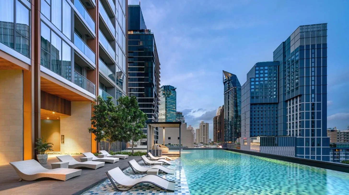 a swimming pool with lounge chairs and a city skyline at Oakwood Suites Bangkok in Bangkok