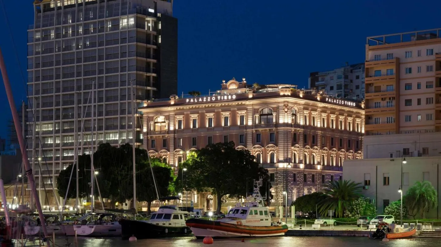a large building with boats in a harbor at night at Palazzo Tirso MGallery Cagliari in Cagliari