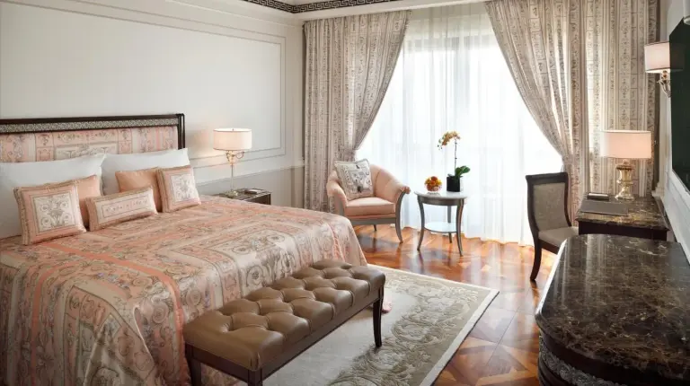 a bedroom with a bed and a chair and a window at Palazzo Versace Dubai in Dubai