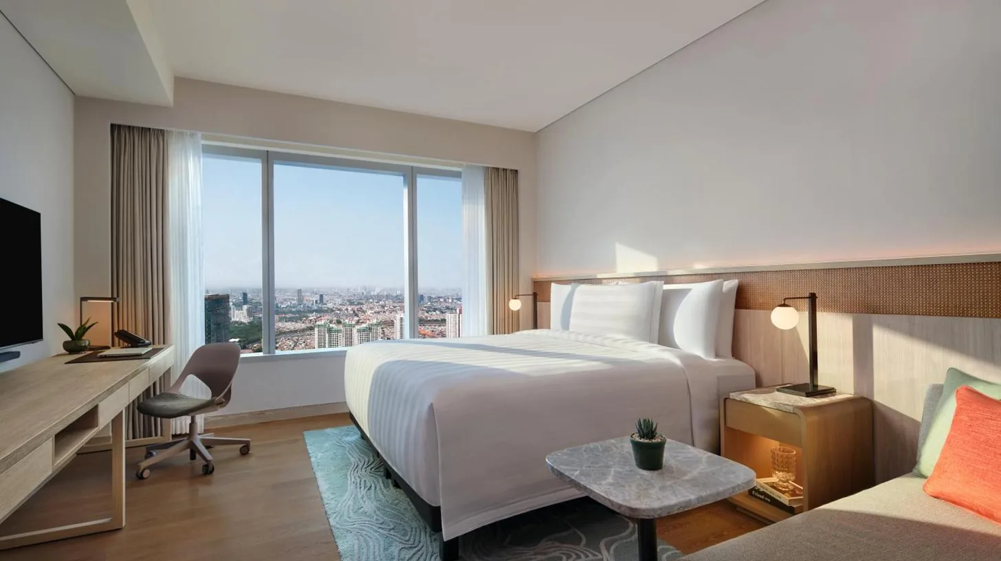 a hotel room with a bed and a desk and a window at PARKROYAL Serviced Suites Jakarta in Jakarta