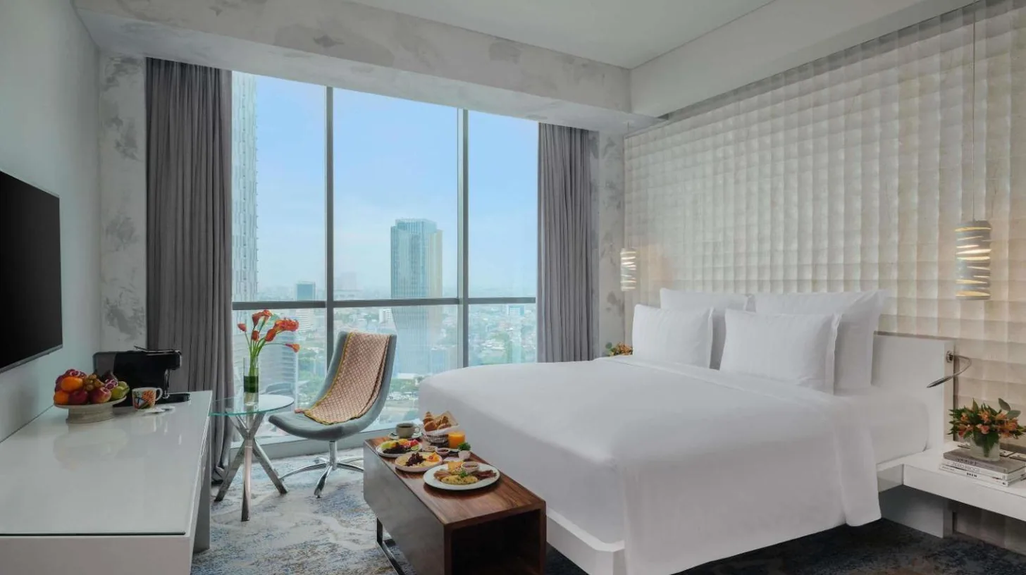 a hotel room with a large white bed and a desk at Pullman Jakarta Central Park in Jakarta