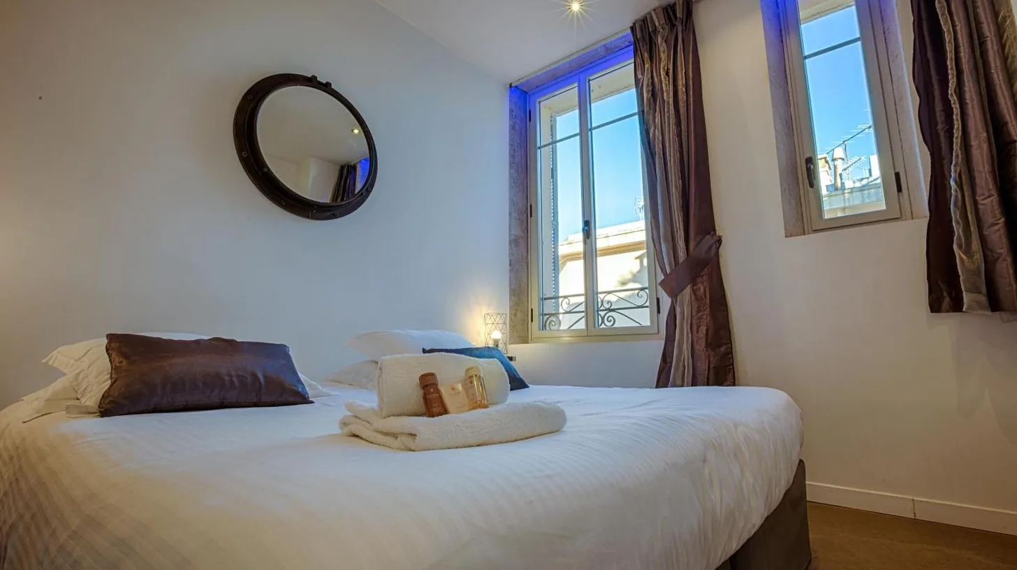 a bedroom with a bed with a mirror and windows at Residence du Louvre - Apartments - Prime location Palais & Croisette - Luxury Stay by LRA Cannes in Cannes