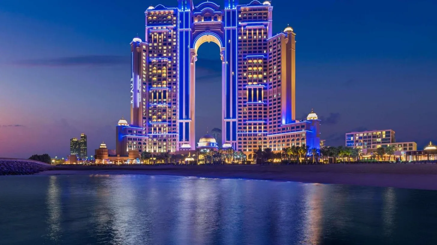 a tall building with blue lights on the water at night at Rixos Marina Abu Dhabi in Abu Dhabi