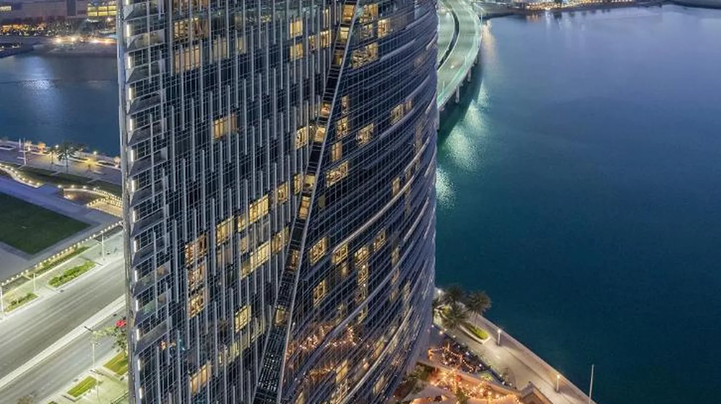 a tall building with a sign on it next to a body of water at Rosewood Abu Dhabi in Abu Dhabi