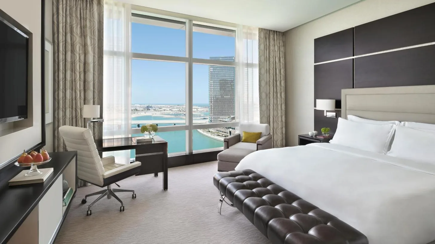 a hotel room with a bed and a desk and a large window at Rosewood Abu Dhabi in Abu Dhabi