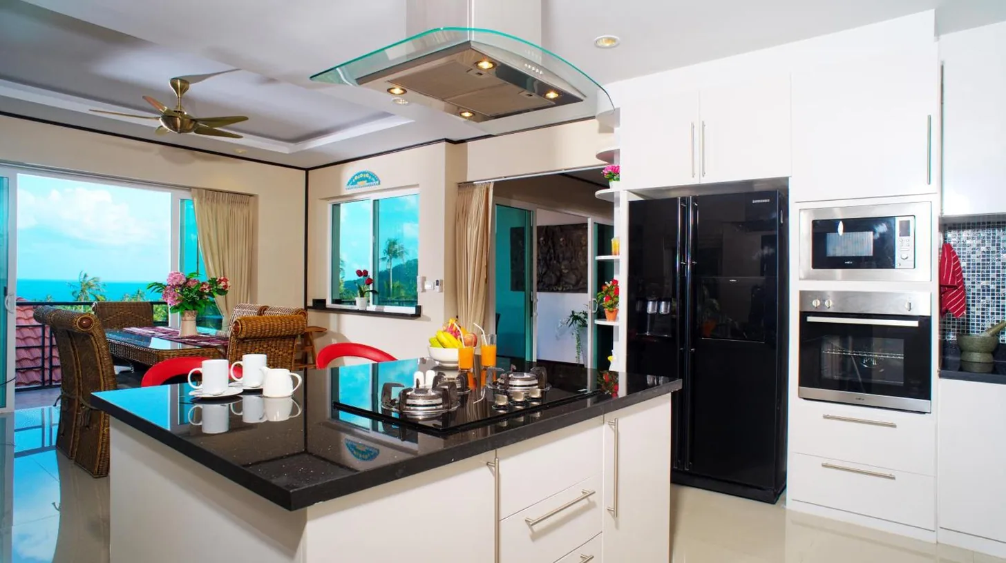 a kitchen with white cabinets and a black refrigerator at Samui Sunrise Seaview Villa in Chaweng