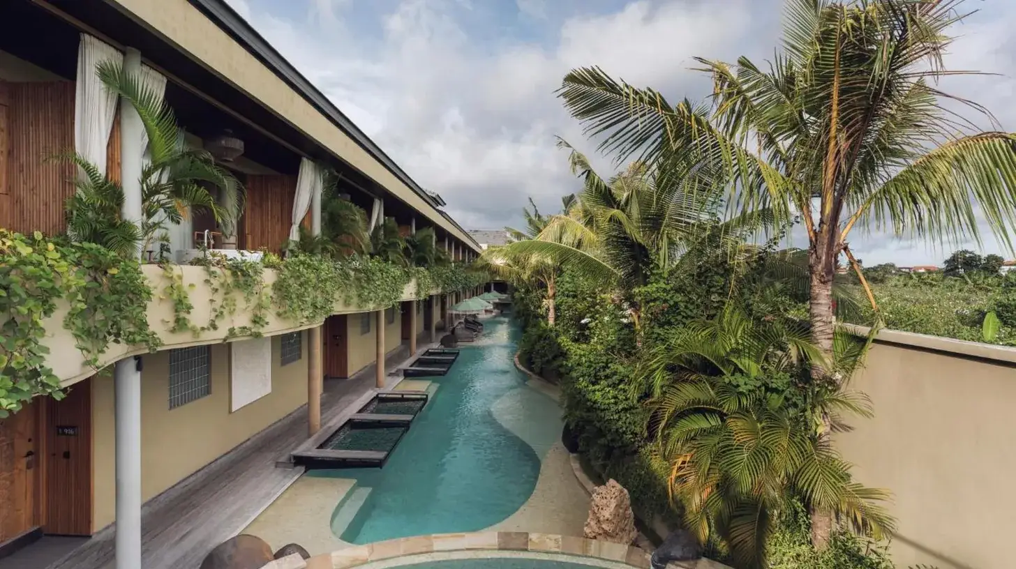 a hotel corridor with a swimming pool and palm trees at Sini Vie Resort & Spa Seminyak by Ini Vie Hospitality in Seminyak