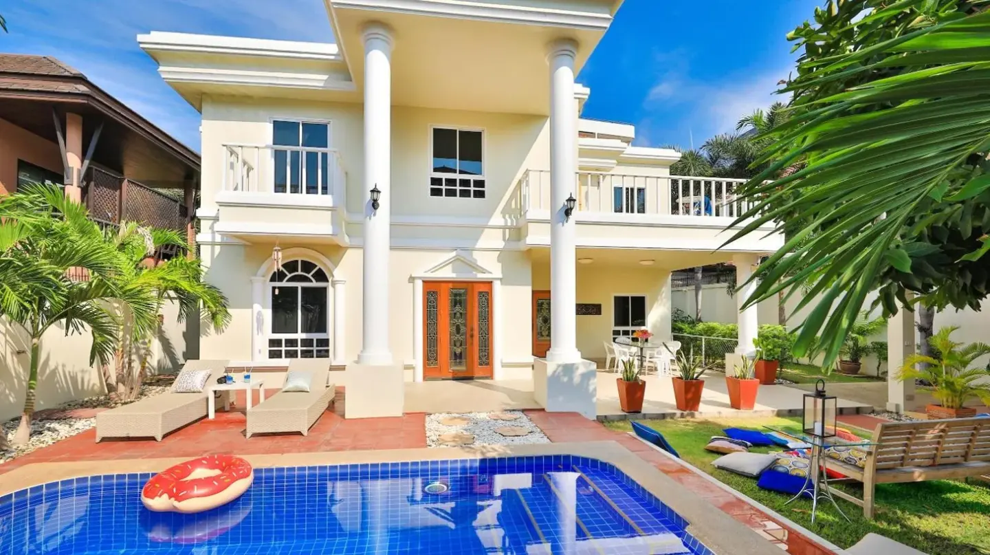 a villa with a swimming pool in front of a house at Sweet Villas Pattaya in Pattaya South