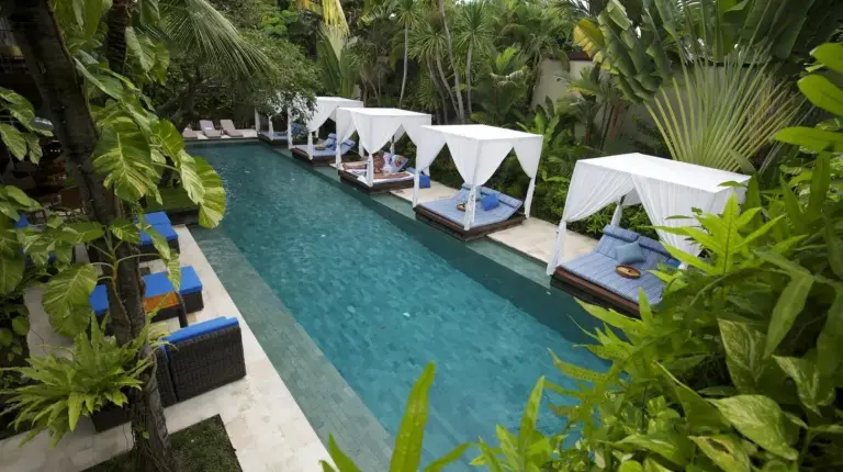 ein Pool mit Stühlen und Sonnenschirmen in einem Resort im The Elysian Boutique Villa Hotel in Seminyak