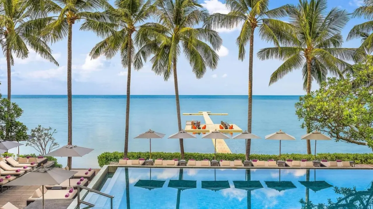 a swimming pool with palm trees and the ocean at The Lamai Samui in Lamai
