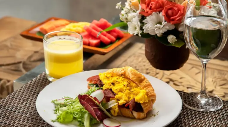 a table with a plate of breakfast food and a glass of wine at The Luxury Collection